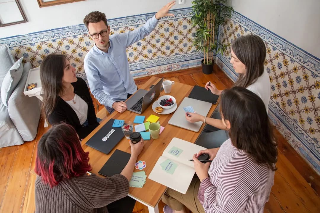 Grupo de pessoas sentadas ao redor de mesa de madeira em reunião colaborativa