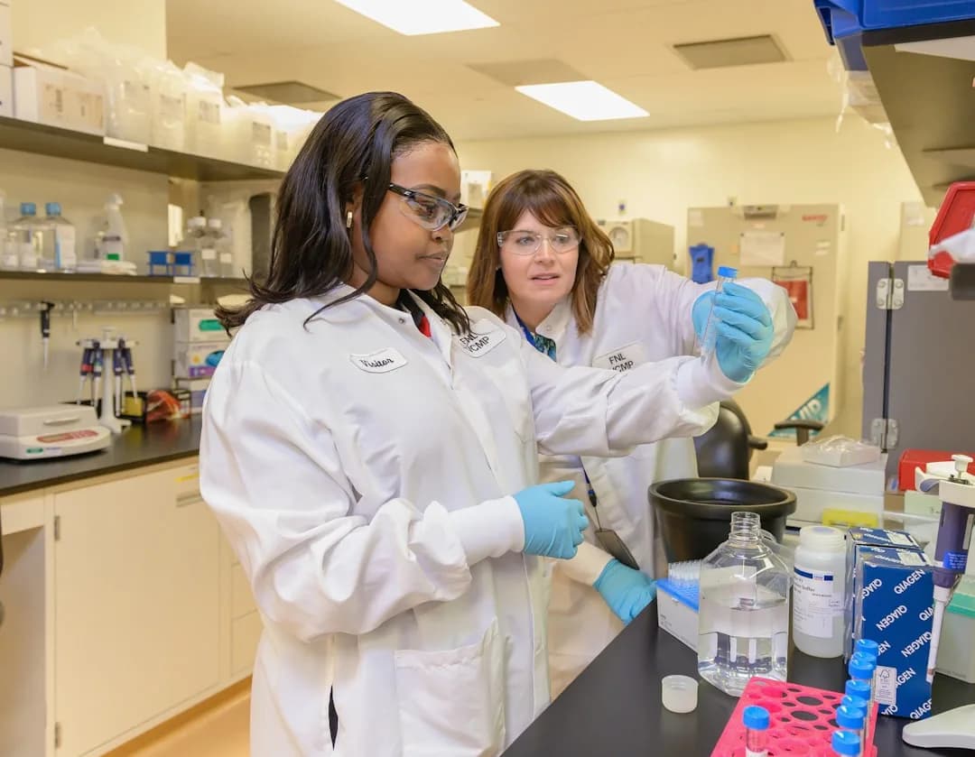 Duas pesquisadoras em jaleco branco trabalhando em laboratório científico