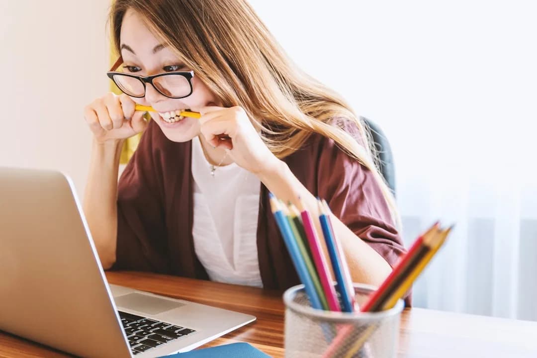 Mulher pensativa mordendo lápis em frente ao computador enquanto pesquisa teste vocacional online